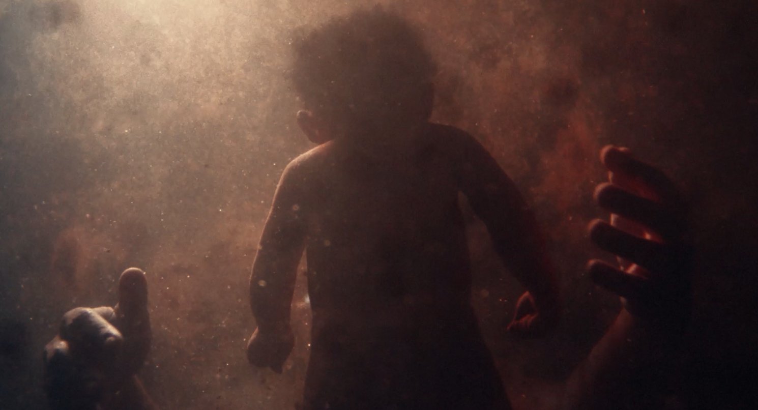A child reaching through a haze of dust as hands reach towards them, from the Avatar showreel